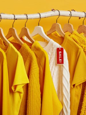 Clearance sale in clothes store. Yellow and bright clothing on hangers during Black Friday. Big discounts on sweaters. Knitted jumper on rack with tag. Buy stylish outfit for low price only today